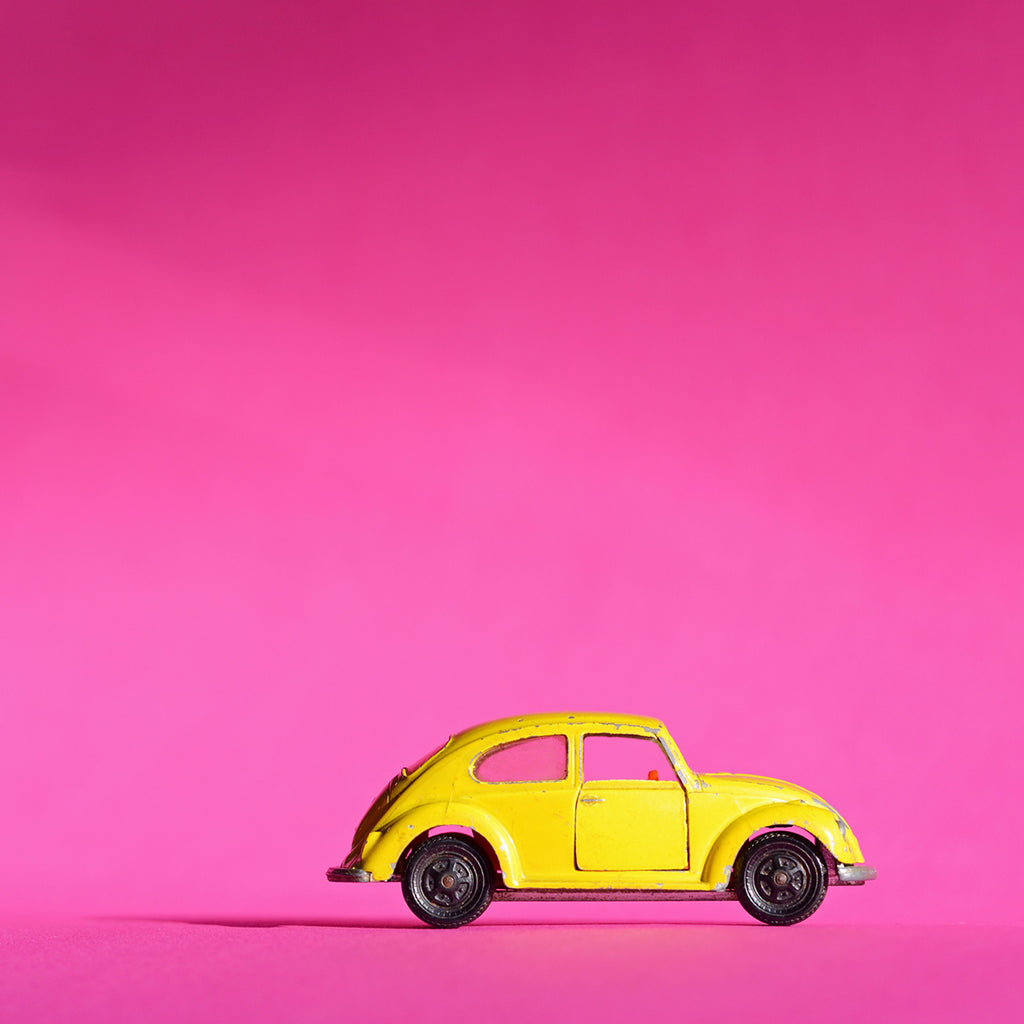 gelber VW Käfer fotografiert vor pink