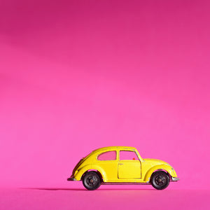 gelber VW Käfer fotografiert vor pink